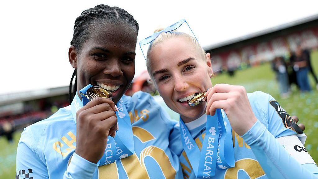 Khadija Shaw and Alex Greenwood with their Women's Super League winners medals in their mouths while smiling