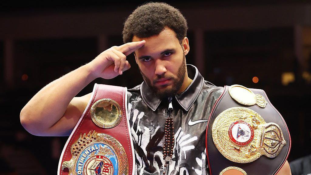 Moses Itauma salutes the camera with his belts around his shoulders