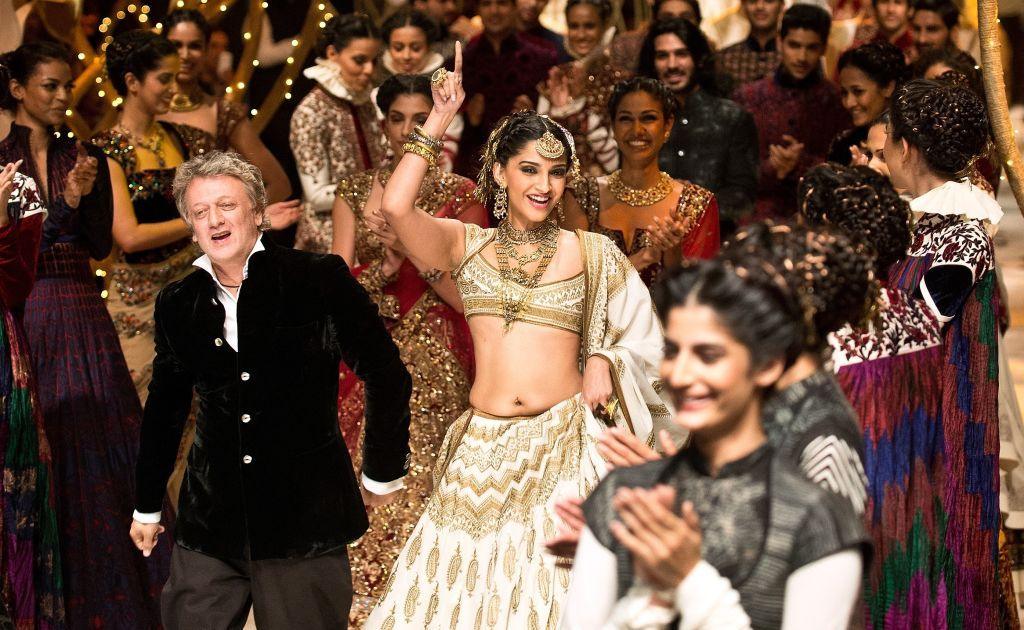 Bollywood actress Sonam Kapoor shows clothes designed by Rohit Bal during Indian Bridal Fashion Week in 2013. Bal walks with her through a crowd