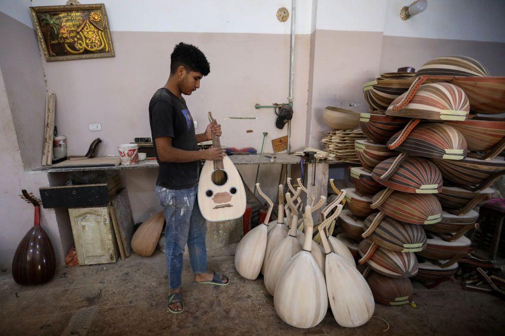  Young man holding Traditional Oud Instrument at workshop belonging to Khaled Azzouz, a longtime maker of the traditional oud instrument. The instruments are piled up in rows next to a wall.