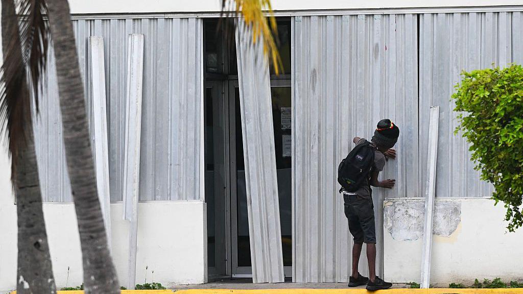 A man installs metal storm shutters on the front of a building