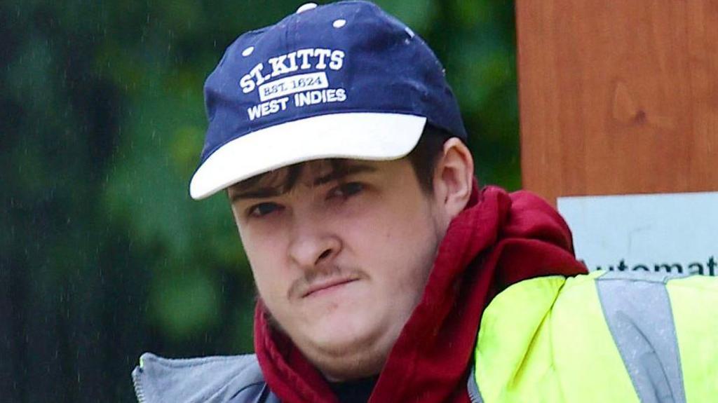 Mr Sterritt outside court. He's wearing a navy and white baseball cap, a red hoodie and a high-vis jacket 