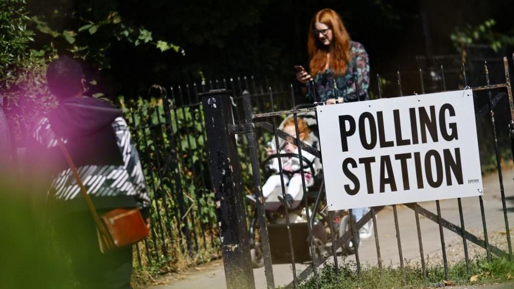 A woman pushing a pushchair in front of a polling station sign