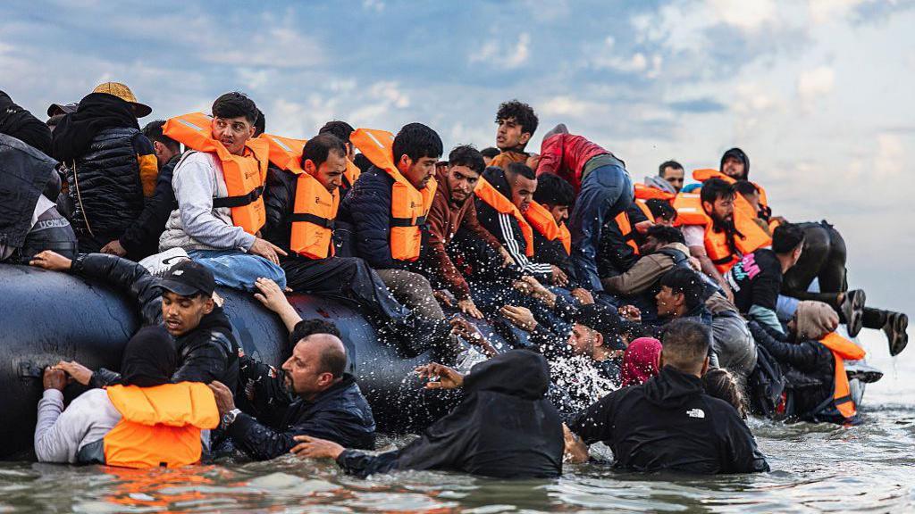 Migrants in orange lifejackets try to board a black inflatable smuggler's boat from the water off the beach of Gravelines, in an attempt to cross the English Channel.