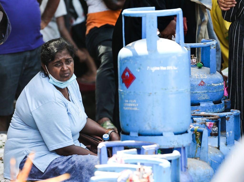 A woman sits next to a pile of liquefied petroleum gas canisters