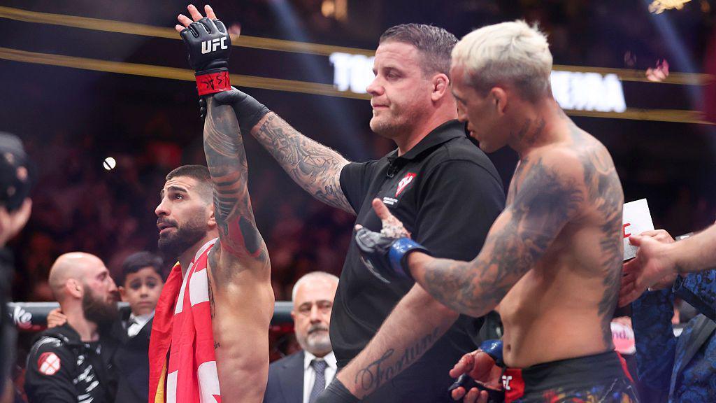 Ilia Topuria has his hand raised by the referee as Charles Oliveira applauds