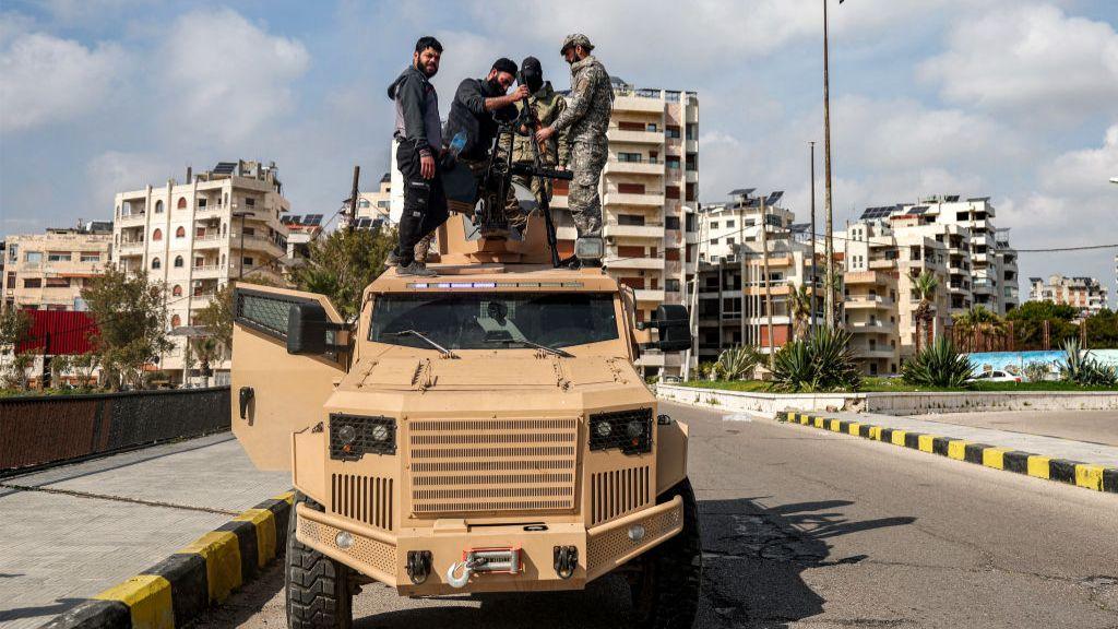 Four men in uniform stand on top of military vehicle fixing a long range gun