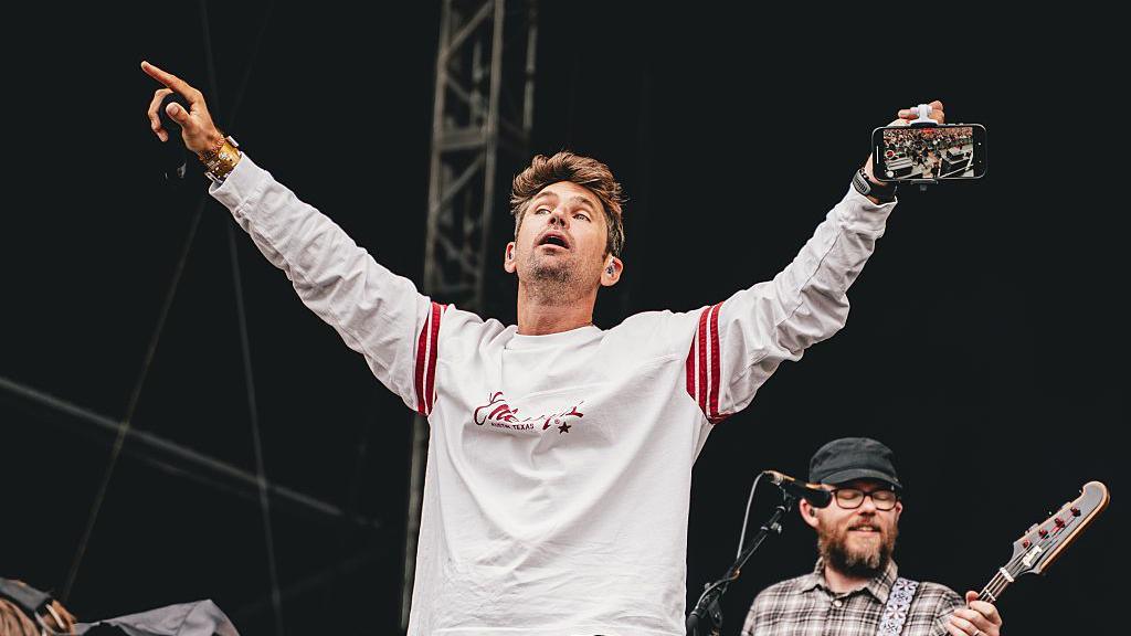 Roy Stride of Scouting For Girls performs onstage during Tramlines at Hillsborough Park. He holds out his arms to the crowd.