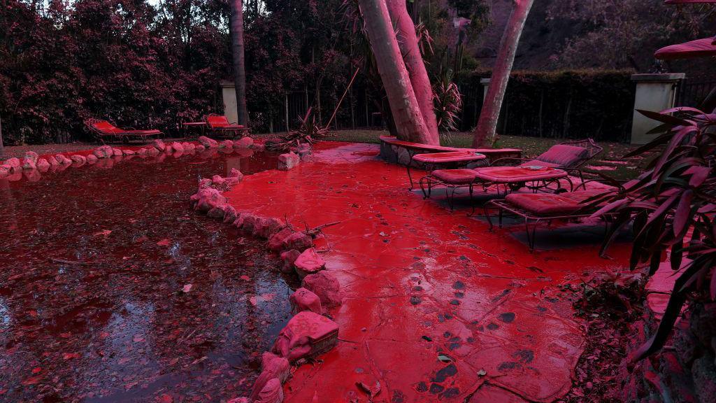 Fire retardant covers a pool and lounge chairs after being dropped from a firefighting aircraft battling the Palisades Fire.