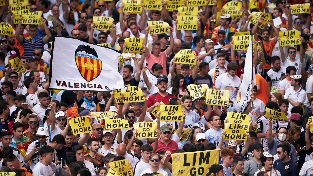 Hundreds of people, several of whom are holding 'LIM GO HOME' signs, protest before a game in Valencia