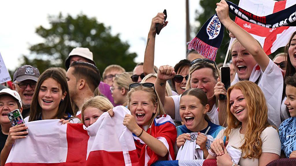 Fans holding flags and posters wait at Southend Airport to see England's Women return