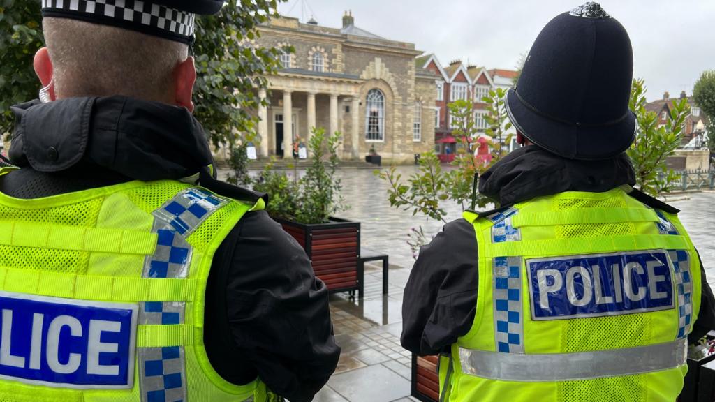 Two police officers facing away from camera, looking out to a square in Salisbury, where it has been raining