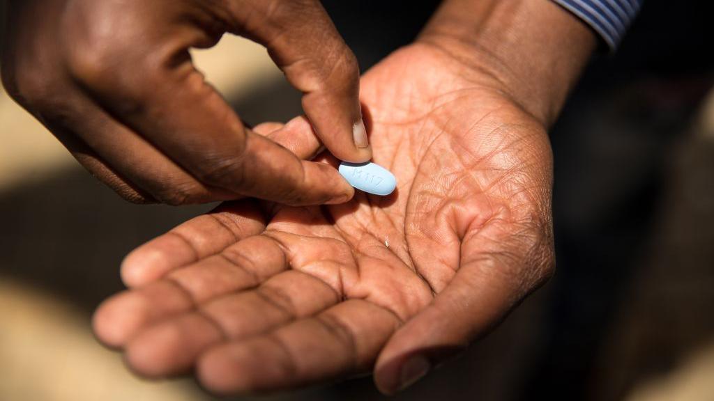 Close-up of a man's hands with a large, oval-shaped light blue pill in one of his palms.