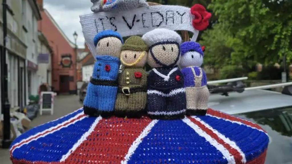 A postbox topper with a red, blue and white base marking the Union Flag and then figures, including sailors and a member of the army, on top of it.