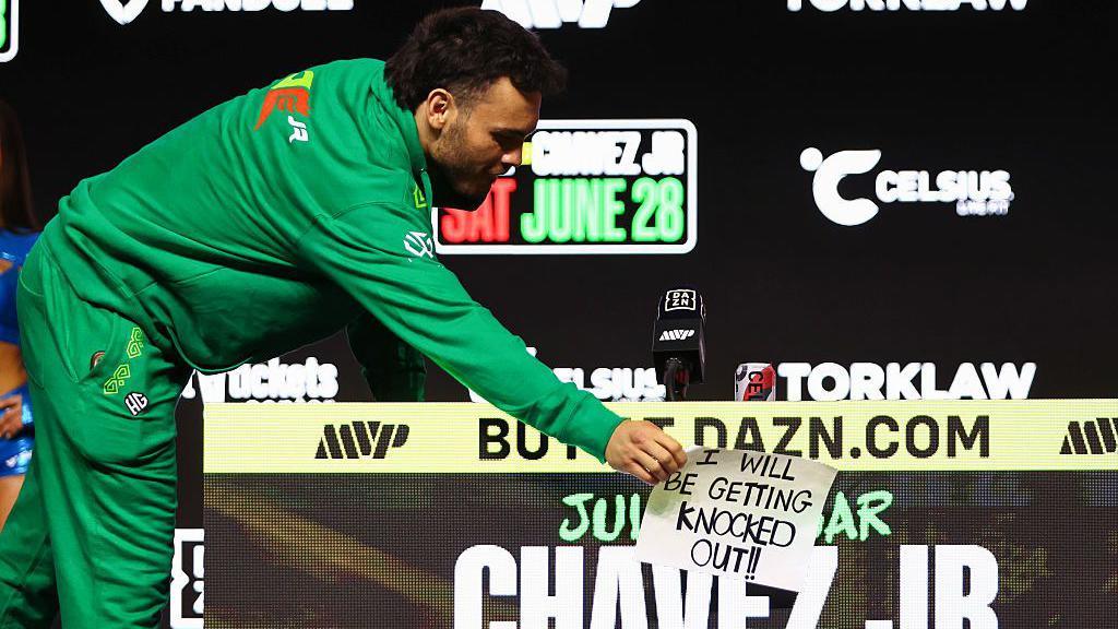 Julio Cesar Chavez Jr peels off a sign saying 'I will be getting knocked out' from his table at a news conference