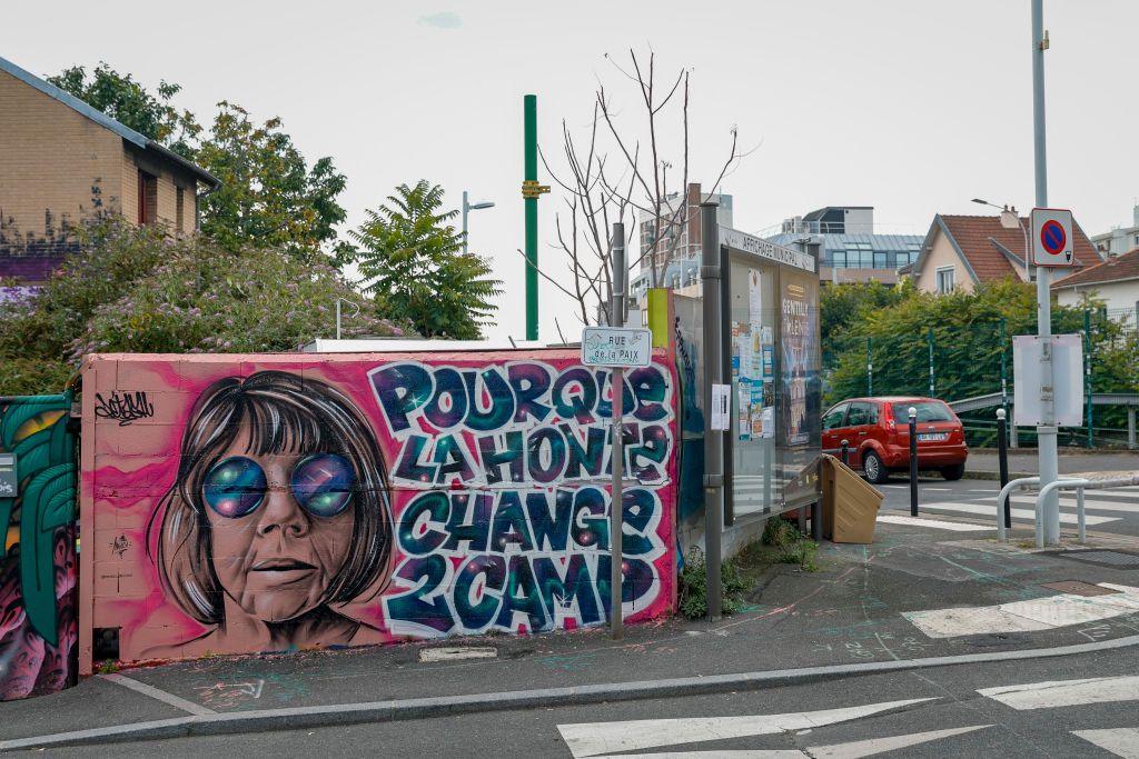 A mural near a pedestrian crossing, with a picture of a woman with a short bob and round sunglasses with the words: "Shame must change sides"