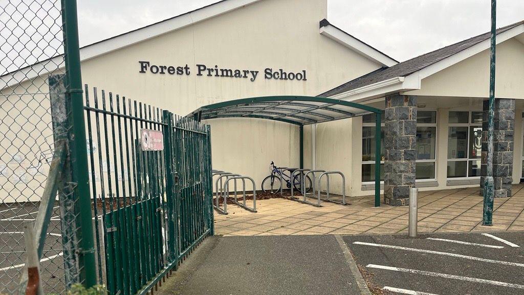 A yellow single-story school building with a bike rack outside and Forest Primary School sign.