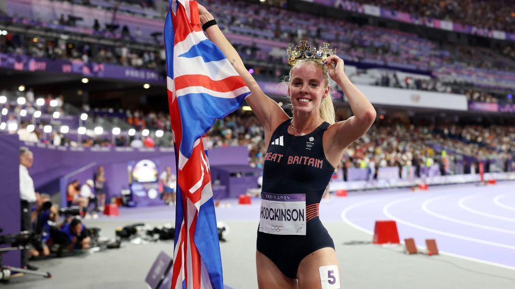 keely hodgkinson holding a british flag and a crown on her head