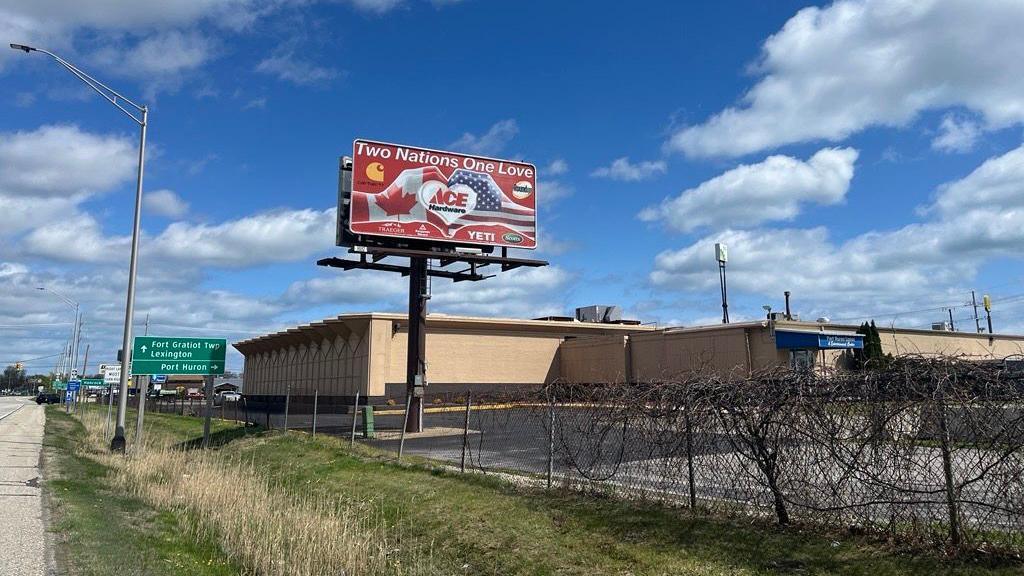 Billboard with two hands making a heart, one hand has the Canadian flag and the other has the American flag. The sign reads "Two nations, One Love".