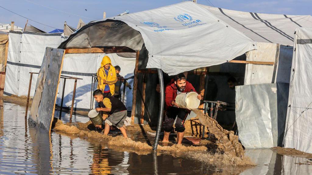 Displaced Palestinians use buckets to stop their tents being flooded by rain and sewage in al-Mawasi, near Khan Yunis, southern Gaza (1 January 2025)