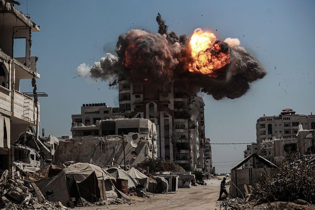 A large explosion rocks a tower block, orange flame and black smoke visible. 