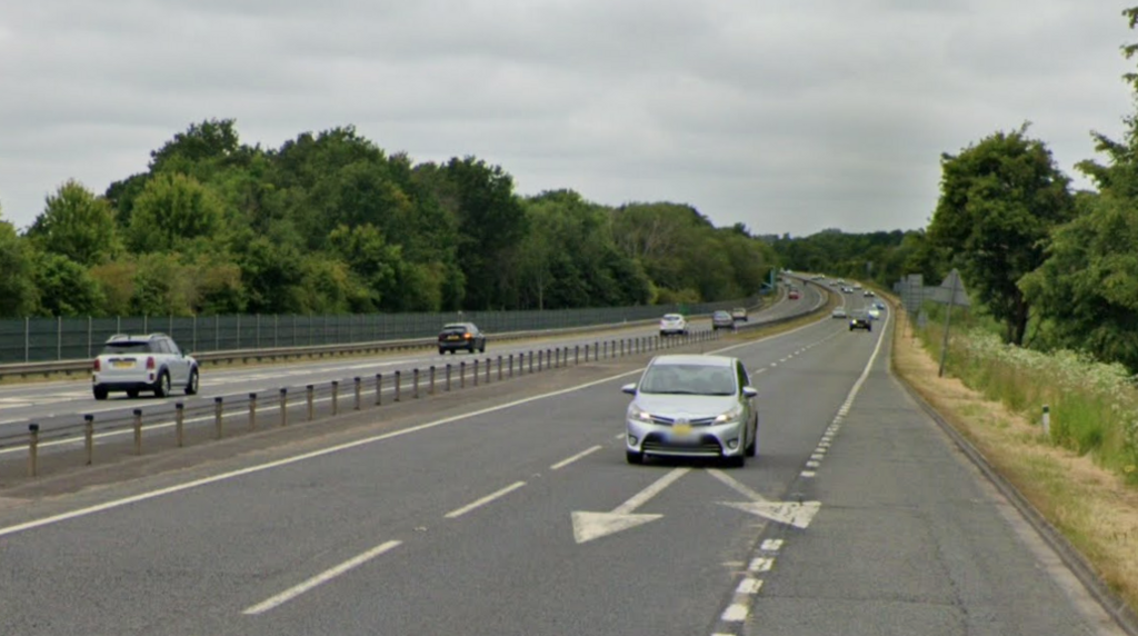 A Google Street View image of a dual carriageway. Greenery can be seen on either side of the road, which has a metal barrier in the middle. It has fairly light traffic on it.