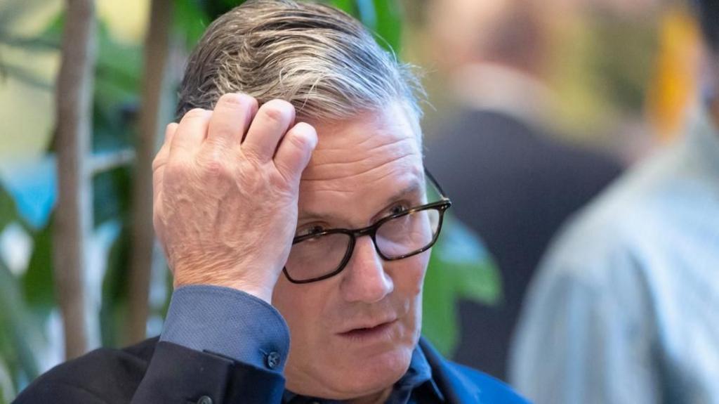 Starmer touches his head with his right hand 