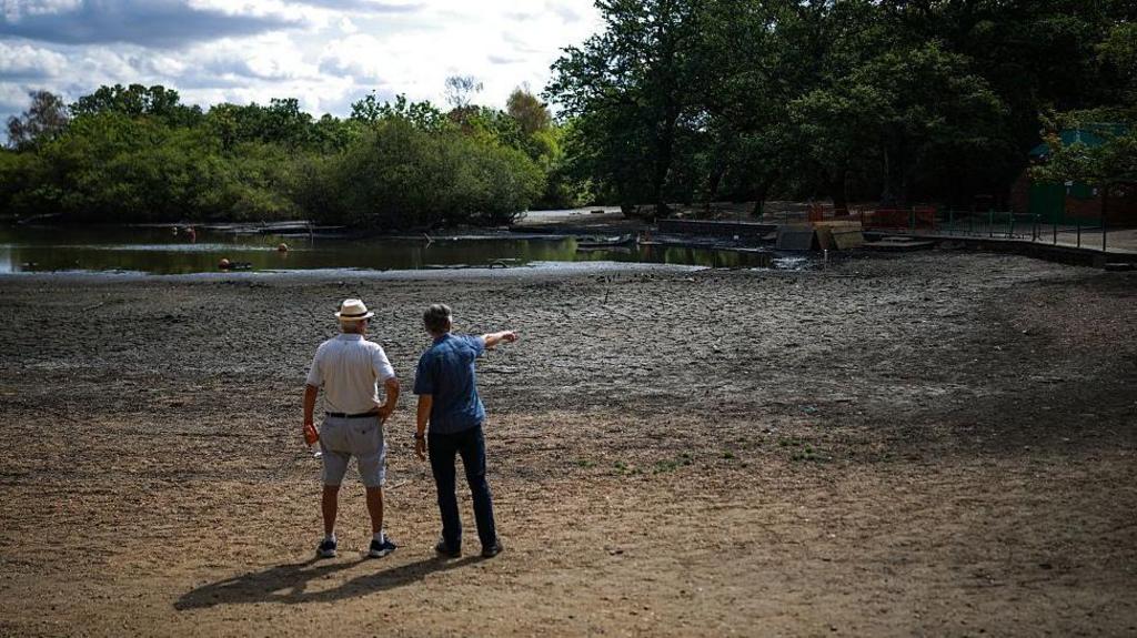 People look out over the dried and cracked bed of the depleted Hollow Pond and Leyton flats near Wanstead, east London.