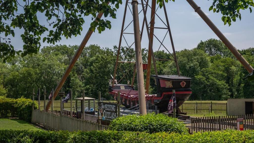 A pirate ship ride is surrounded by greenery on a sunny day.