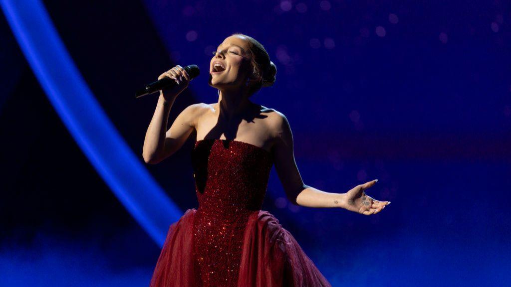 Ariana Grande in a red sparkly dress singing into a handheld microphone at the Oscars in March 2025