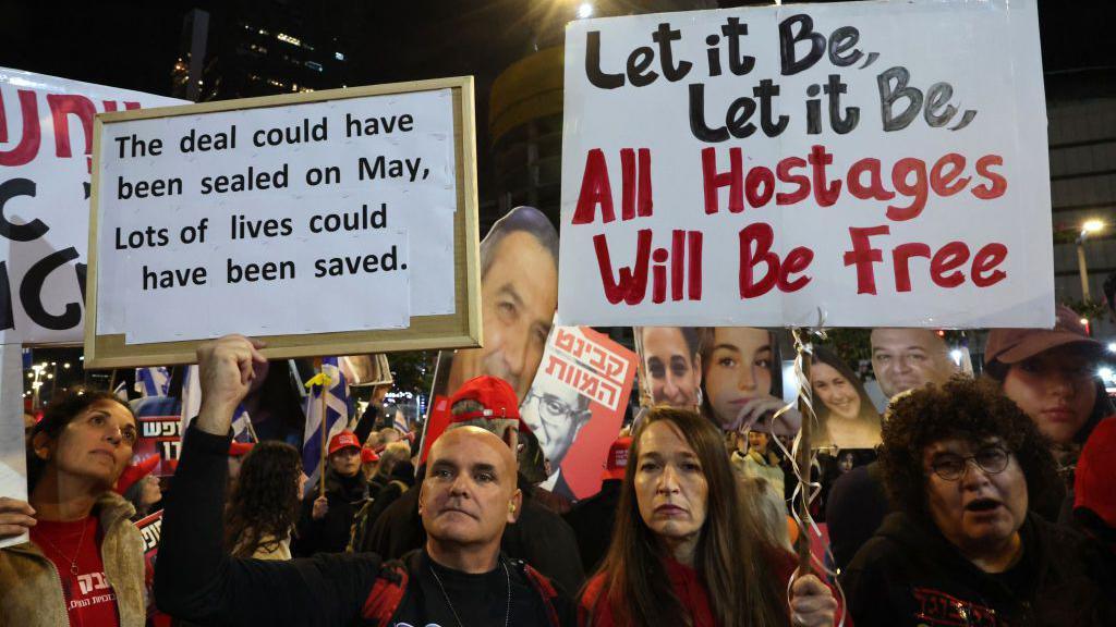 Pro-hostage deal demonstrators hold signs in a demonstration saying 'the deal could have been sealed on May, lots of lives could have been saved' and 'let it be, let it be, all hostages will be free'.