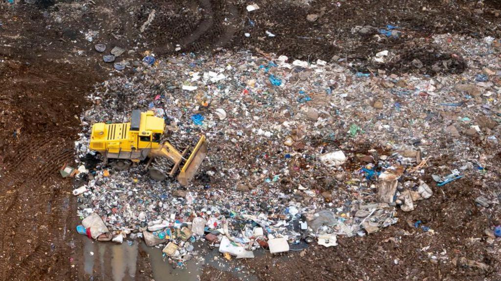 A digger is seen moving waste at the tip