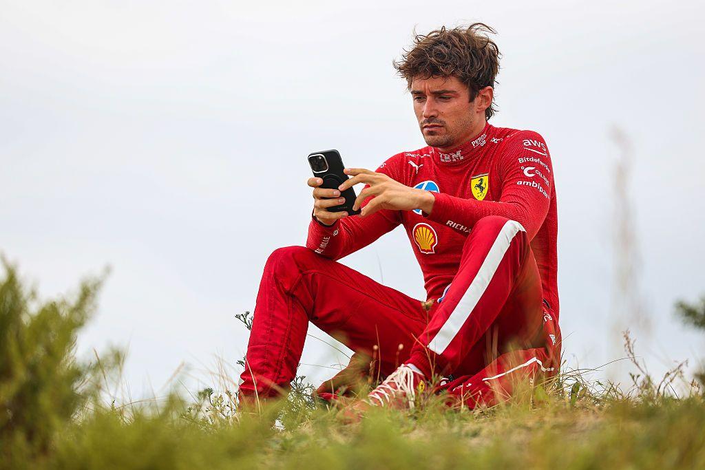 Ferrari's Charles Leclerc on a mobile phone while sitting on a sandbank after retiring from the Dutch Grand Prix