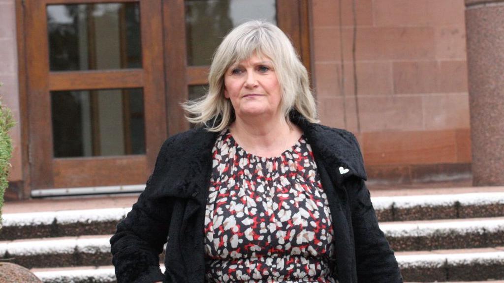 A woman wearing a red, white and black dress, and a black coat  leaves a court building