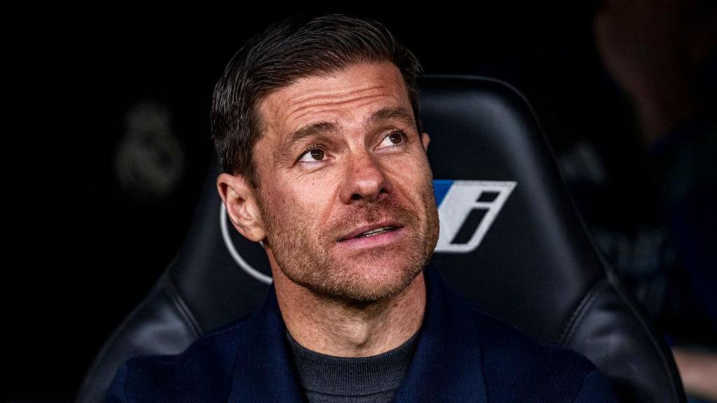 Xabi Alonso smiling while sat in the Real Madrid dugout