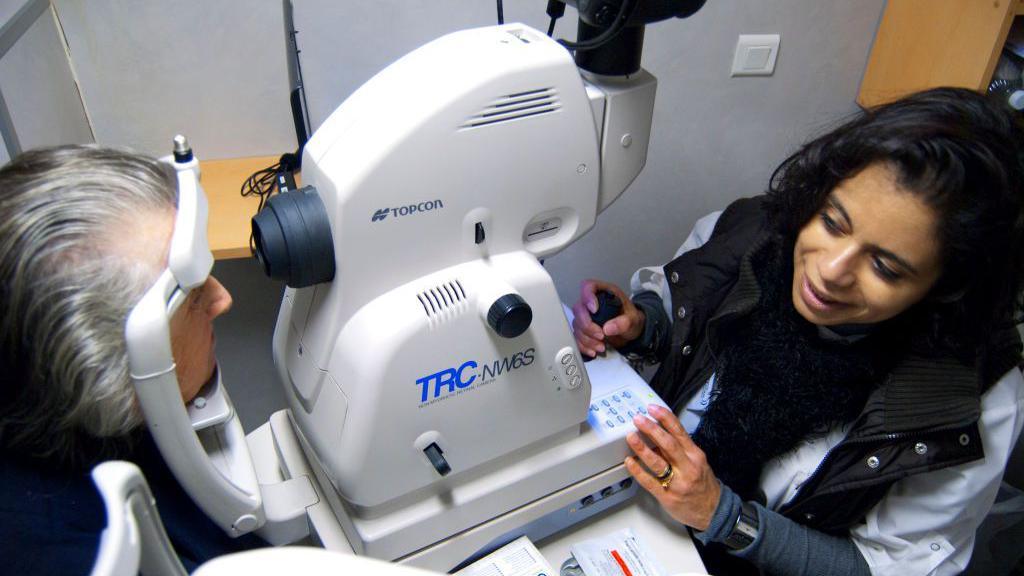 A patient looks into an eye scanner, while a health work looks on.