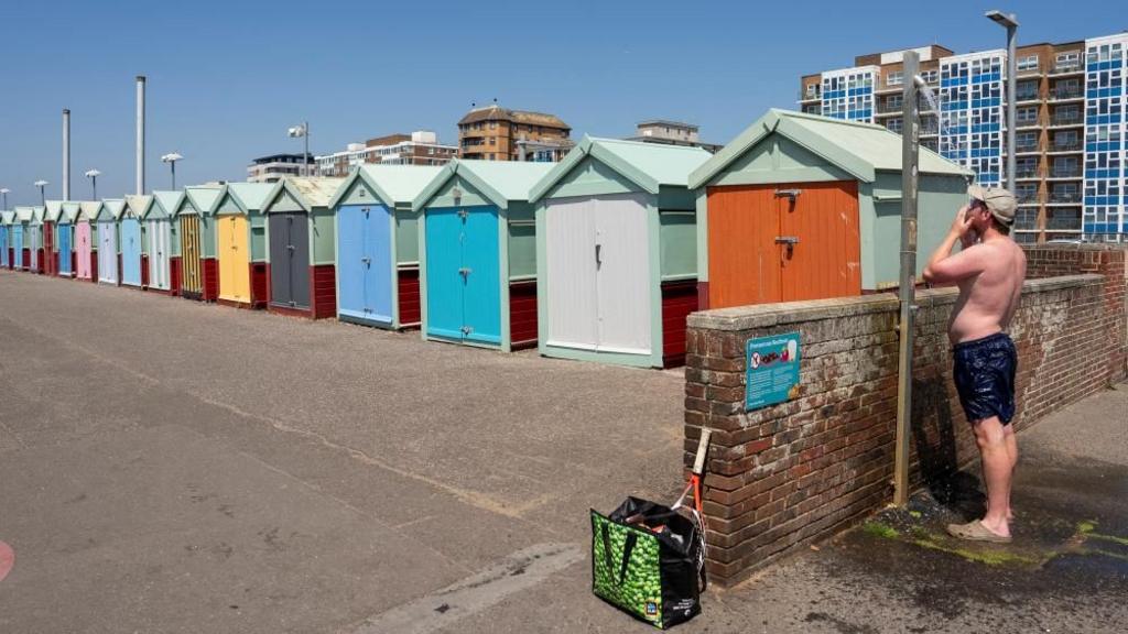 A man has a shower near some beach huts. 