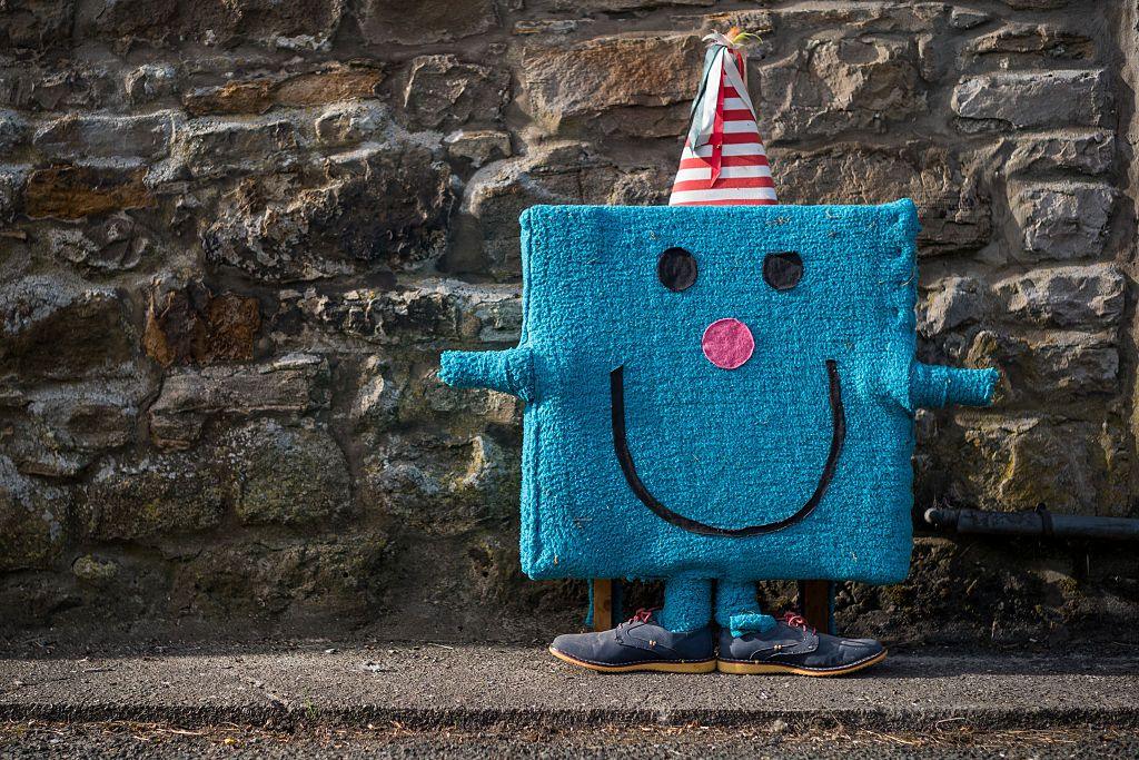 A model of Mr Birthday from the Mr Men book series can be seen seemingly covered in blue carpet. The character has a face stuck on and is wearing a red and white striped party hat.