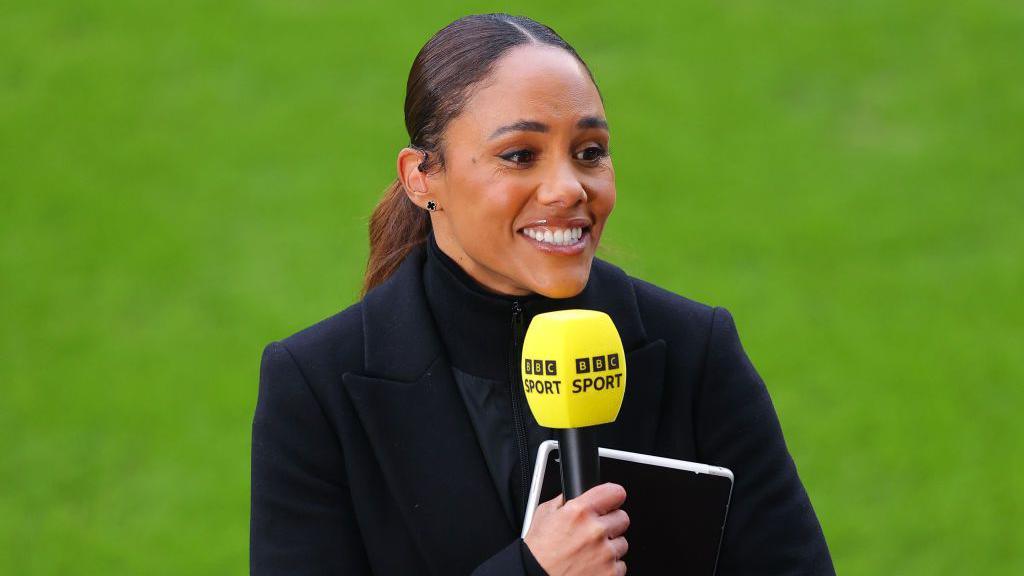 Alex Scott holding a BBC microphone