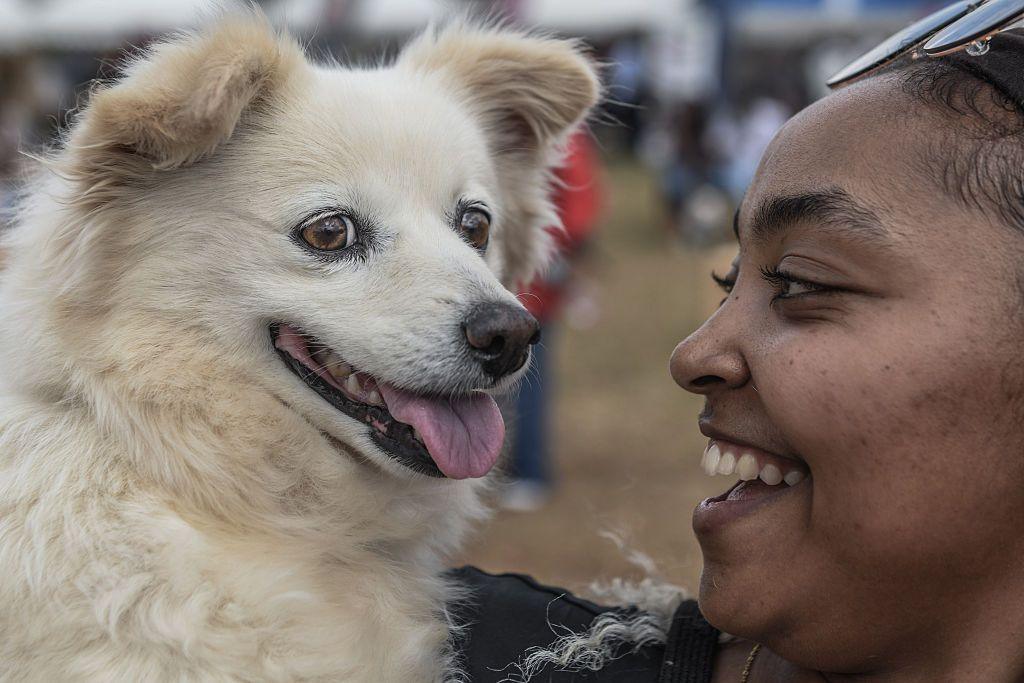 A woman holds her happy-looking dog up and smiles.