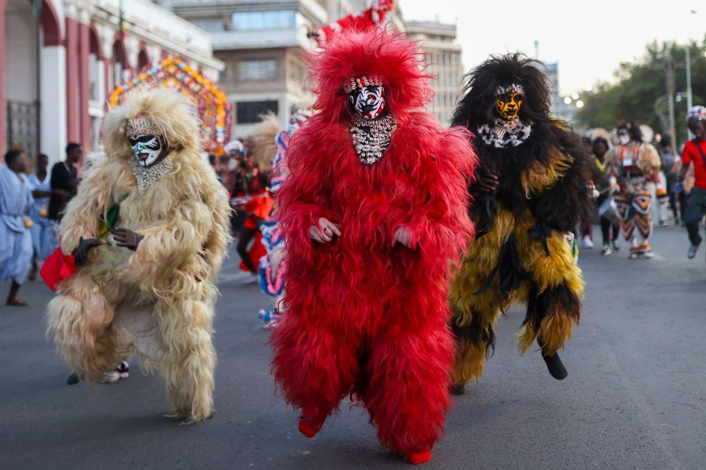 People marching down a road wearing voluminous costumes of different colours.