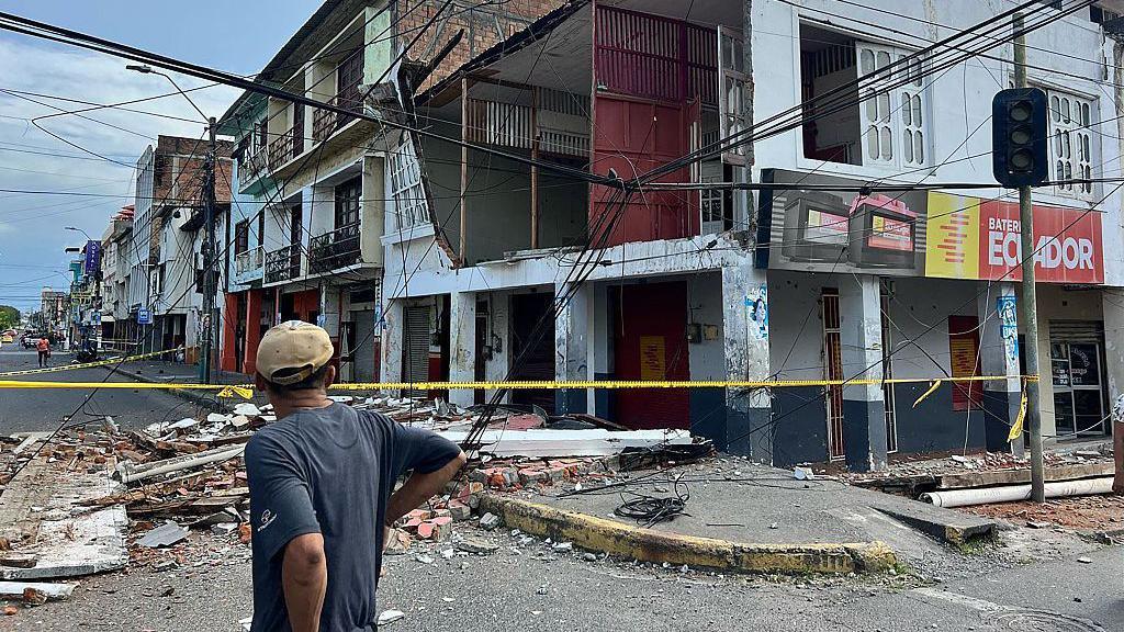A man surveys the damage done to some buildings, one of which's facade has fallen off onto the road, after an earthquake struck the port city of Esmeraldas