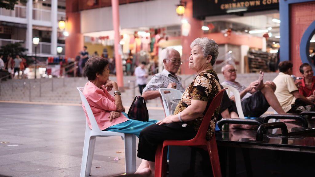 Old people sitting on plastic chairs in an open space