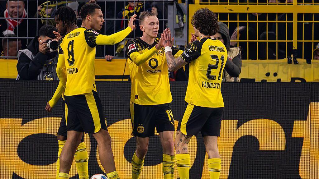 Borussia Dortmund players celebrate Dortmund's second goal against Borussia Monchengladbach. The players are wearing yellow kits with black trim and black shorts.