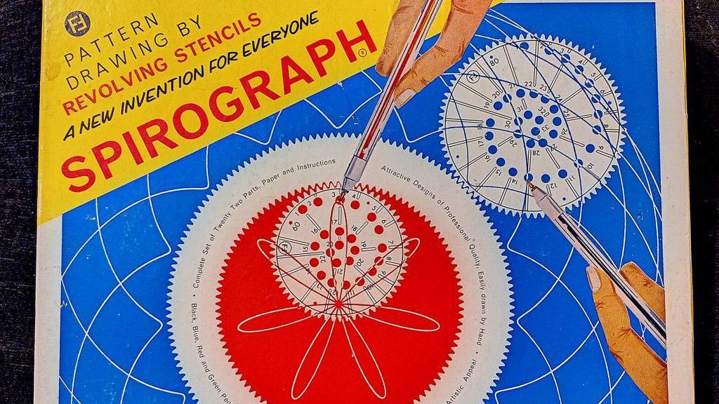 Vintage Spirograph set cover featuring a yellow banner with promotional text and the word 'SPIROGRAPH' in bold red letters. Below, two illustrated hands use pens and circular stencils to draw patterns on a blue background. A large white gear with smaller gears inside displays intricate red and white designs. Surrounding text highlights the educational and creative benefits of the toy.