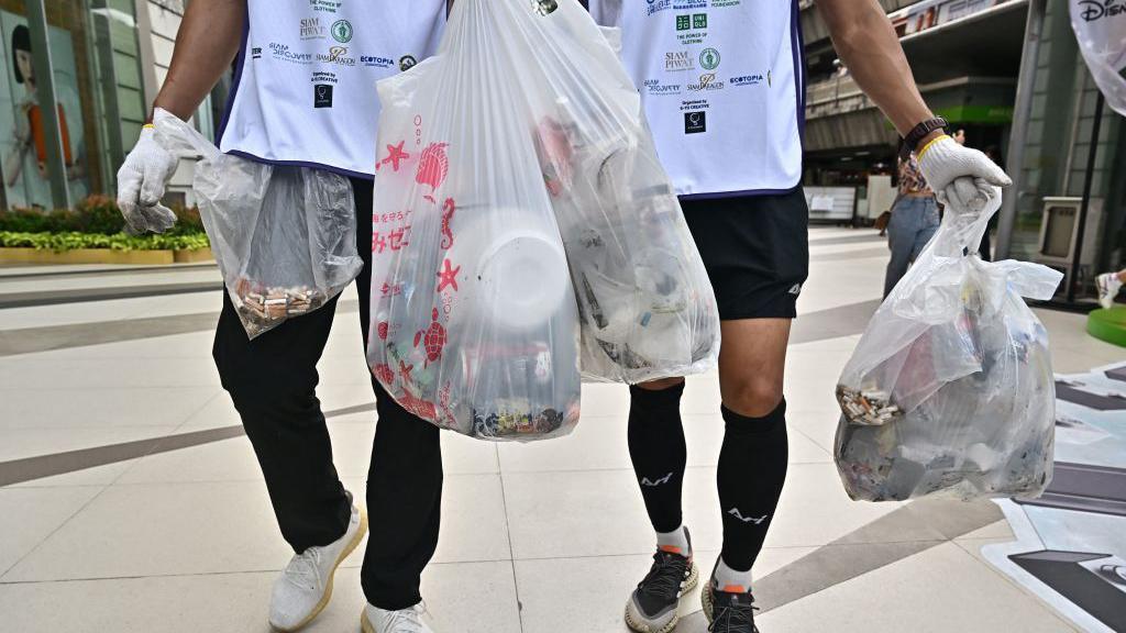 People are seen walking carrying clear plastic bags filled with rubbish