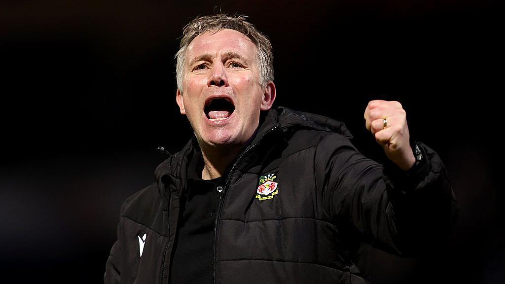 Phil Parkinson in a black Wrexham coat celebrates with a punch in the air