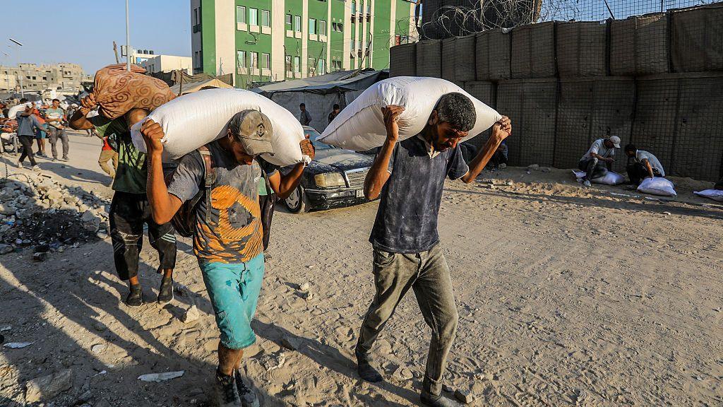  Palestinians, struggling with hunger amid ongoing Israeli attacks, carry the bags of flour they received at the aid distribution point distributed by the World Food Programme (WFP) in Khan Yunis, Gaza