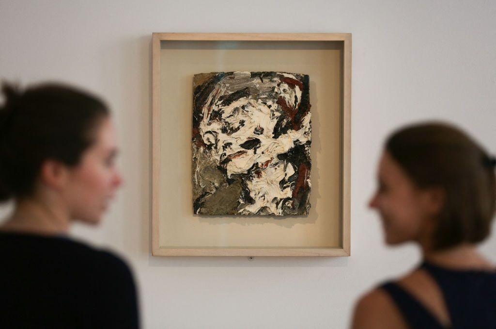 Sotheby's employees pose for a picture in front of an artwork owned by the David Bowie, Head of Gerda Boehm by Frank Auerbach, painted in 1965. It is an abstract-looking artwork, primarily white and dark colours. 