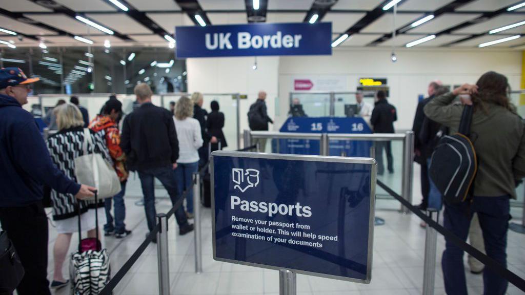 A sign saying 'passports' at the UK border - with a sign saying 'UK border' in the background as people queue up